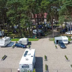 Kampery i przyczepy kempingowe na żwirowym polu namiotowym w lesie sosnowym. Widok z lotu ptaka na sea camp Rogowo.