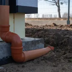 Pomarańczowe rury do odprowadzenia wody z rynien, połączone kolankami, biegną wzdłuż fundamentu domu i wkopane są w ziemię.