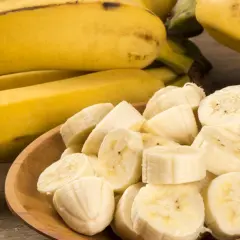 Kawałki banana na drewnianej misce, obok całe owoce. Idealna przekąska, gdy zastanawiasz się nad banan kcal.