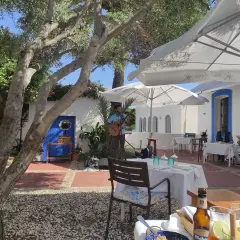 Un músico toca la guitarra en el patio de el pozo de los frailes restaurantes. Mesas puestas bajo sombrillas blancas invitan a disfrutar.