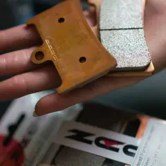 Main d'une personne tenant des plaquettes de frein neuves, prêtes pour le rodage. Le logo "DZ" est visible sur l'une d'elles.