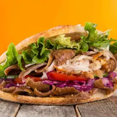Kebab w bułce z mięsem, warzywami i sałatą na drewnianym stole.