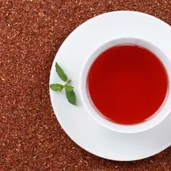 Taza de té rojo con menta, rodeada de hojas secas. Descubre los te rojo beneficios para tu bienestar.