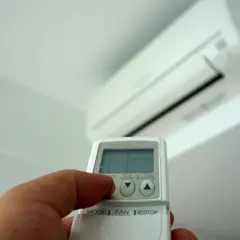 Mano sujetando un control remoto de aire acondicionado, ajustando la temperatura para controlar cuanto gasta un aire acondicionado.