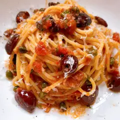 Ein Teller Spaghetti Puttanesca, garniert mit Oliven, Kapern und geriebenem Parmesan.