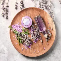 Sur un plateau en bois, des brins de lavande fraîche et séchée, des cristaux violets et une petite bouteille de liquide pour faire bouillir de la lavande.