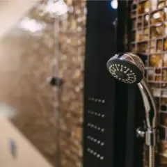 Une colonne de douche moderne avec un pommeau chromé et des jets intégrés, prête à installer dans une salle de bain aux murs mosaïqués.