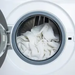 Tambour de machine à laver rempli de linge blanc prêt pour un lavage éclatant avec de l'eau de javel pour blanchir le linge en machine.