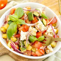 Frischer zucchini-salat mit feta, Tomaten, roten Zwiebeln und Basilikum, garniert mit Kräutern.