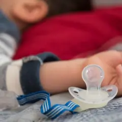 Dziecko śpi z rączką obok smoczka, który może powodować odparzenia.