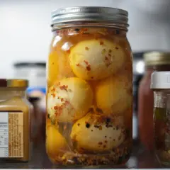Un bocal rempli d'œufs au vinaigre, épicés et conservés dans un liquide ambré, se tient au premier plan.