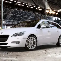 Biały Peugeot 508 SW na jasnych felgach, z widocznym rozmiarem opon, stoi w opuszczonej hali przemysłowej.