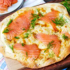 Flammkuchen mit Lachs und Dill, frisch gebacken auf einem Holzbrett.