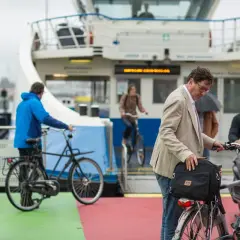 Man met fiets op veerboot, een ongeluk fietser in de verte.