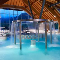 Piscina interna con cascata, lettini e vista sulle montagne. Un luogo ideale per rilassarsi nelle terme in Slovenia vicino al confine italiano.