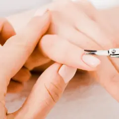 Unghie curate: una mano assiste l'altra con forbicine per unghie, mostrando come si fanno le unghie perfette.