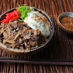 A delicious Yoshinoya beef bowl recipe, featuring tender beef, onions, a fried egg, pickled ginger, and green onions, ready to be enjoyed.