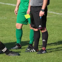 Sędzia piłkarski trzyma żółtą kartkę, gotowy do podjęcia decyzji. Chcesz wiedzieć, jak zostać sędzią?