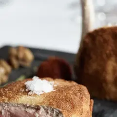 Ein knuspriges Kalbsschnitzel, italienisch zubereitet, mit feinen Beilagen auf einem dunklen Teller.