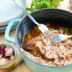 Szarpana wieprzowina w garnku, rozrywana widelcami, obok czosnek i papryczka chili.