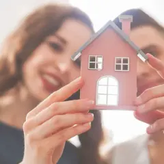 Coppia felice tiene in mano una casetta rosa, simbolo della loro futura casa cointestata.