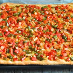 Coca mallorquina recién horneada, cubierta con pimientos rojos y verdes picados y cebolla.