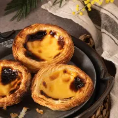 Trois délicieux flans portugais, dorés et caramélisés, sur un plateau en métal.