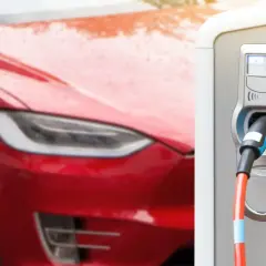 Czerwona Tesla podłączona do ładowarki. Zastanawiasz się, jak długo ładuje się Tesla? Czas zależy od modelu i ładowarki.