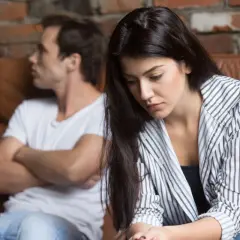 Una donna triste seduta su un divano, mentre suo marito non la desidera e le dà le spalle.