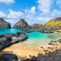 Rajska plaża na Fernando de Noronha z turkusową wodą, skalistymi formacjami i samotną postacią kąpiącą się w oceanie.