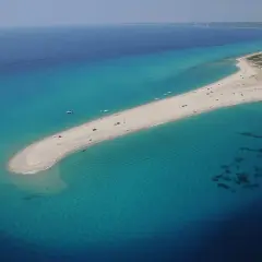 Piękna plaża na Chalkidiki, idealna na wakacje po przylocie na lotnisko. Woda turkusowa, piasek złoty, łodzie na morzu.