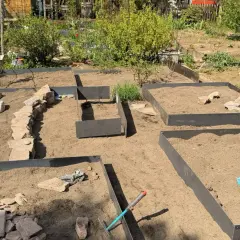 Gartenanlage mit Hochbeeten und naturnahen Gartenwegen aus Steinen. Werkzeuge liegen bereit.