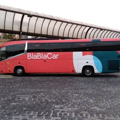Un bus BlaBlaCar rouge et gris est garé sur une place pavée sous un auvent.