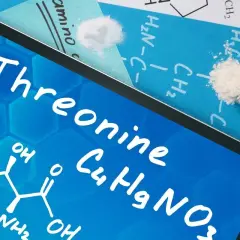 Tablet z napisem "Threonine" i wzorem chemicznym. Obok proszek w probówce i na kartce.