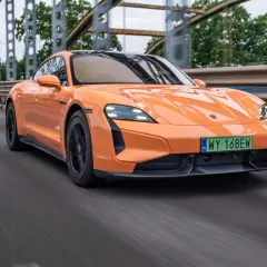 Pomarańczowy Porsche Taycan Turbo S pędzi po moście, jego sportowy design podkreślony przez dynamiczne linie.