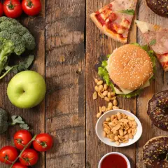 Gesunde Lebensmittel wie Brokkoli, Tomaten und ein Apfel stehen im Kontrast zu Junkfood wie Pizza, Burger, Pommes und Donuts.