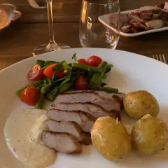 En tallrik med saftigt grillad pluma, serverad med småpotatis, sparris, körsbärstomater och en krämig sås. En härlig måltid!