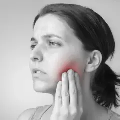Mujer con un bulto en la mejilla que se mueve, tocándose la zona con la mano. El área afectada está resaltada en rojo.