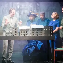 Aktorzy na scenie, prezentujący polskie musicale, gestykulują przy makiecie miasta.