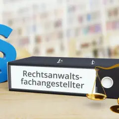 Paragraphen-Symbole, Aktenordner mit "Rechtsanwaltsfachangestellter" und eine Waage. Informationen zum Rechtsanwaltsfachangestellte Gehalt sind hier relevant.