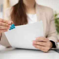Kobieta w jasnym żakiecie trzyma niebieski klips do papieru na białych dokumentach.