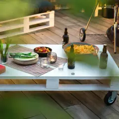 Tavolo fai da te con snack, bevande e candele su un deck di legno, pronto per una grigliata.