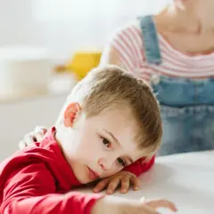 Smutny chłopiec z ADHD opiera głowę na stole, podczas gdy matka kładzie mu rękę na ramieniu.