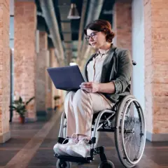 Kobieta na wózku inwalidzkim pracuje na laptopie. Czy lekarz rodzinny może wystawić zlecenie na wózek inwalidzki?