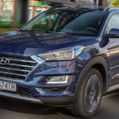 Nowy Hyundai Tucson w ciemnoniebieskim kolorze jedzie ulicą. Elegancka krata wlotu powietrza i nowoczesne reflektory podkreślają jego dynamiczny wygląd.