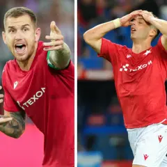 Piłkarz w czerwonej koszulce, Alan Uryga, reaguje na boisku. Po lewej pokazuje palcem, po prawej trzyma się za głowę, być może po kontuzji.