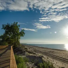 Drewniana kładka wzdłuż plaży, idealna na przejażdżkę rowerową trasą R10. Słońce odbija się w morzu, tworząc piękny widok.