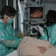 Przygotowanie do gastroskopii: lekarze w zielonych fartuchach i maskach obserwują obraz z endoskopu na monitorze.