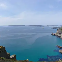 Randonneur victorieux au sommet d'un rocher, bras levés, dominant la mer turquoise et les falaises de GR34 Crozon.