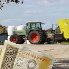 Zielony traktor z przyczepą paszową na tle pola i sterty bel. W tle koparka. Na pierwszym planie polskie banknoty 200 zł. Eudr co to? Inwestycja w rolnictwo.